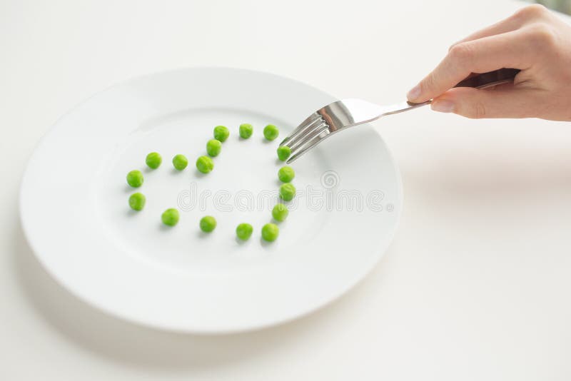 Healthy eating, dieting, vegetarian food and people concept - close up of woman with fork eating peas in shape of heart. Healthy eating, dieting, vegetarian food and people concept - close up of woman with fork eating peas in shape of heart