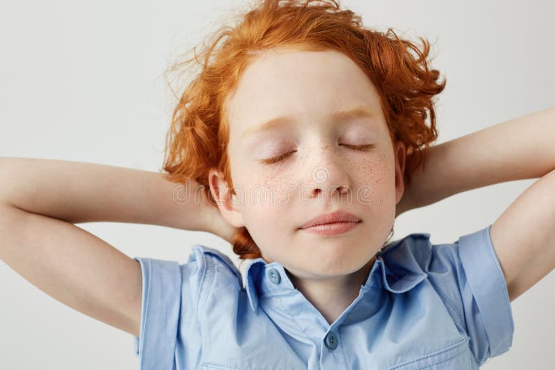 Chiuda su di bello ragazzo sonnolento dello zenzero con capelli ricci e le lentiggini che si tiene per mano dietro la testa con g immagini stock libere da diritti