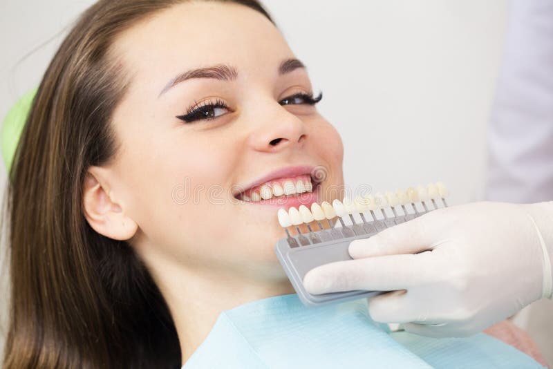 Chiuda sul ritratto delle giovani donne nella sedia del dentista, controlli e selezioni il colore dei denti Il dentista fa il pro immagini stock Chiuda sul ritratto delle giovani donne nella sedia del dentista, controlli e selezioni il colore dei denti Il dentista fa il pro immagini stock