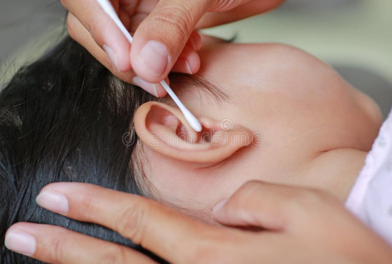 Chiuda sull'orecchio del bambino di pulizia della madre con il tampone di cotone immagine stock libera da diritti Chiuda sull'orecchio del bambino di pulizia della madre con il tampone di cotone immagine stock libera da diritti