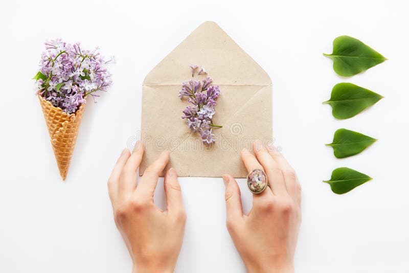 Chiuda sulle mani delle donne che toccano la busta aperta della carta del mestiere riempita di fiori lilla porpora circondati da immagine stock Chiuda sulle mani delle donne che toccano la busta aperta della carta del mestiere riempita di fiori lilla porpora circondati da immagine stock