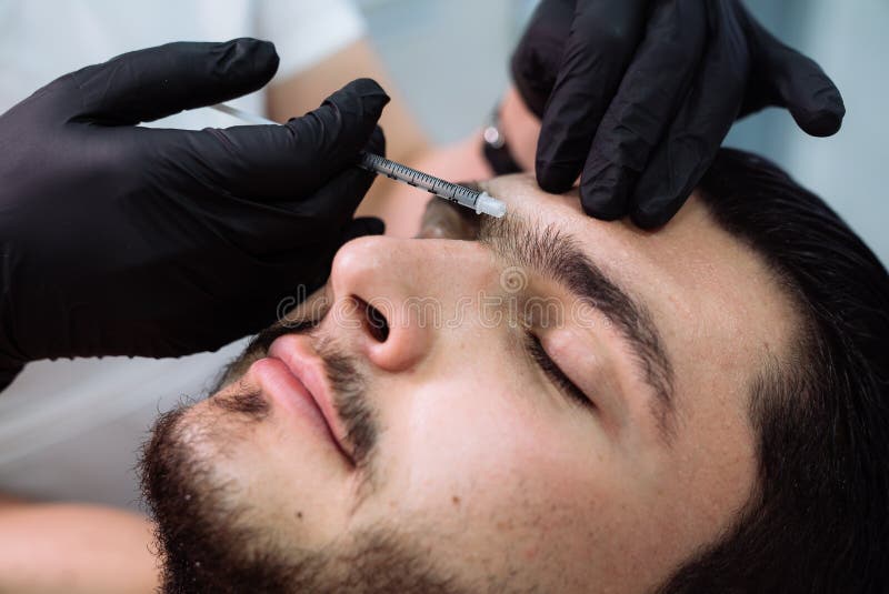 Chiuda sulle mani pazienti maschii del ` s del cosmetologo e del fronte con la siringa durante le iniezioni facciali di bellezza fotografia stock libera da diritti Chiuda sulle mani pazienti maschii del ` s del cosmetologo e del fronte con la siringa durante le iniezioni facciali di bellezza fotografia stock libera da diritti