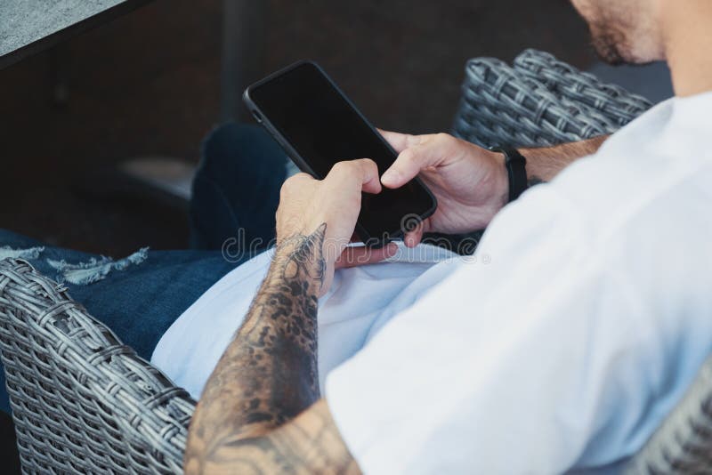 Close up male hands with tattoo holding smartphone with blank copy space screen while connecting to 4g wireless or wifi network, hipster guy using technology sitting at modern coffee shop. Close up male hands with tattoo holding smartphone with blank copy space screen while connecting to 4g wireless or wifi network, hipster guy using technology sitting at modern coffee shop