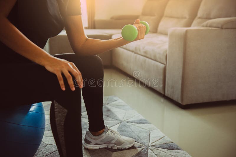 Chiudi la donna che solleva pesi di manichino per l'addestramento a forza mentre sta a casa a pallone Sport e concetto ricreativo