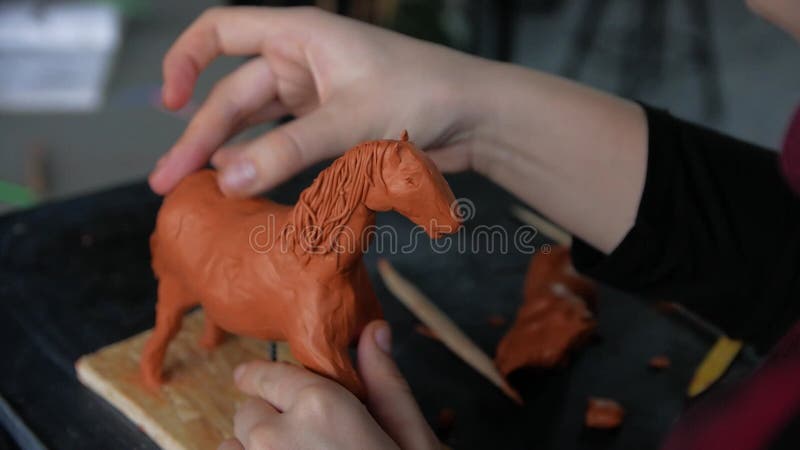 Chiusura delle mani dei bambini che scolpiscono un cavallo dall'argilla modellatrice.