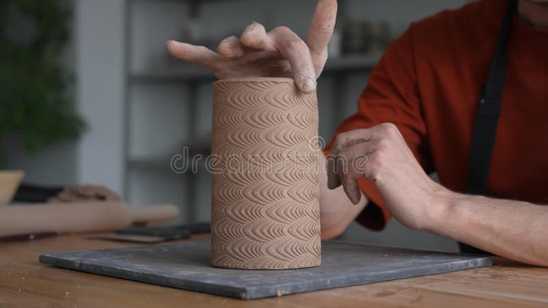 Chiusura delle mani di un uomo che costruisce un cilindro di creta in argilla.