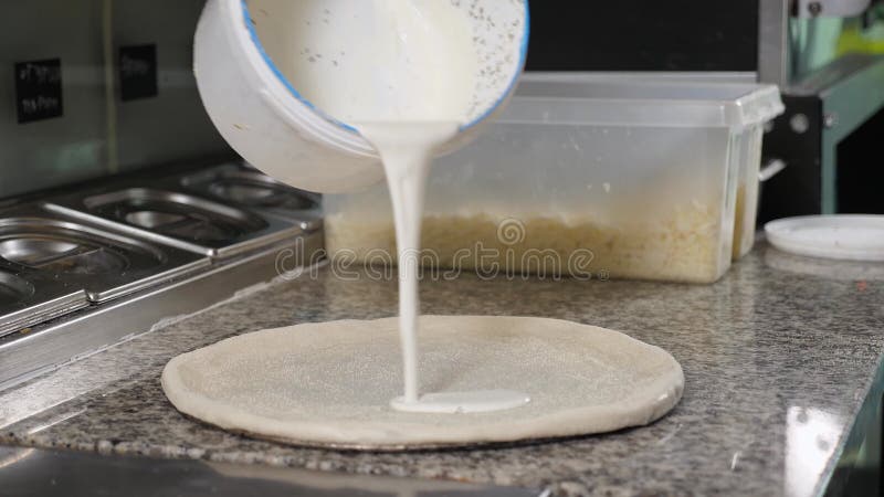 Chiusura dello chef che applica salsa bianca all'impasto per pizza in cucina. video d archivio