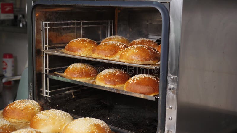 Chiusura dello chef che estrae panini di sesamo al forno per hamburger. video d archivio