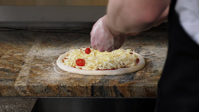 Chiusura dello chef che mette pomodori ciliegie su una pizza con formaggio in pizzeria