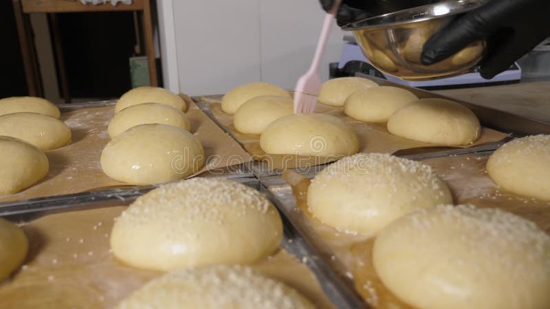 Chiusura dello chef utilizzando un pennello per applicare la miscela di uova ai panini di grattugiamento rotondi. stock footage