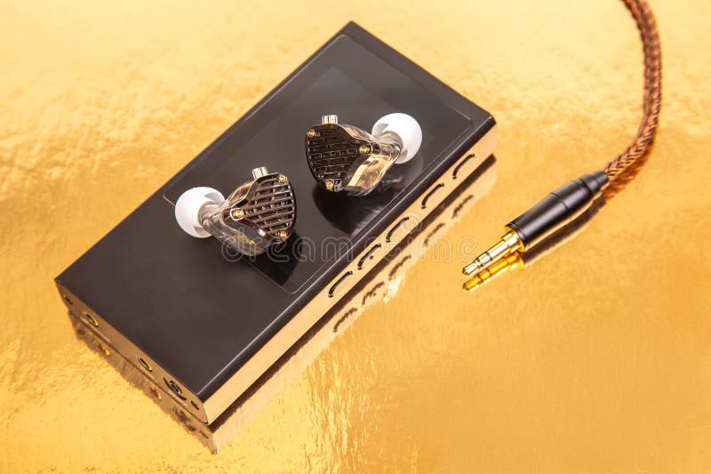 Chiusura di auricolari cablati con cavo intrecciato su un lettore di musica nera elegante che riflette una superficie dorata. Idea immagine stock