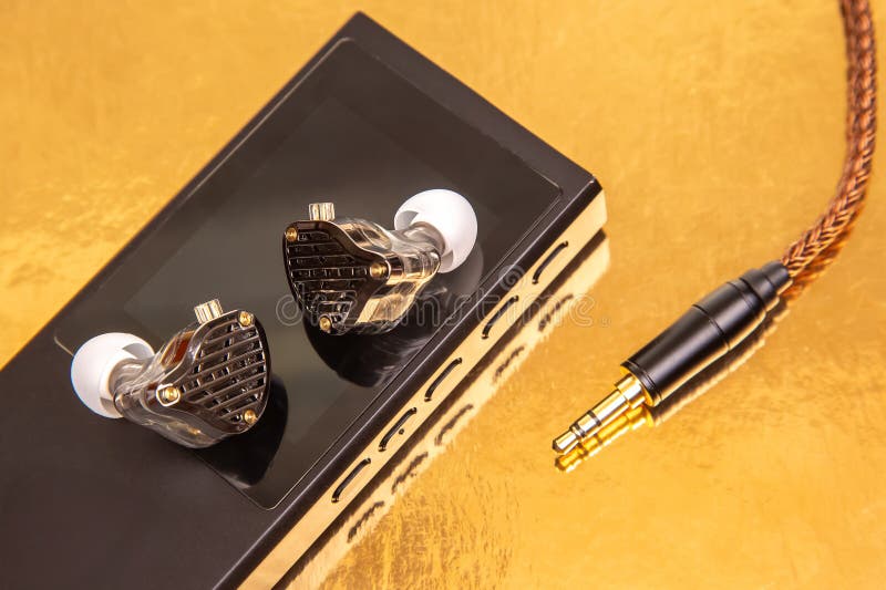 Chiusura di auricolari cablati con cavo intrecciato su un lettore di musica nera elegante che riflette una superficie dorata. Idea immagini stock libere da diritti