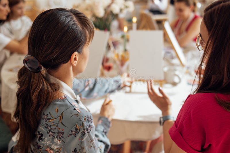Chiusura di giovani donne vestite casualmente in un laboratorio di pittura. amici in una tabella con cavalletti e tele vuote. dall fotografia stock libera da diritti
