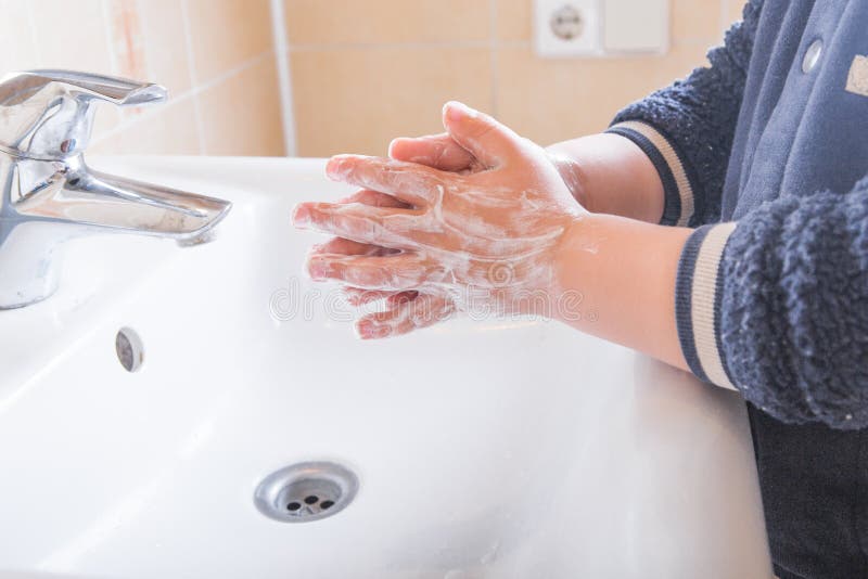 Chiusura di un bambino con le mani insaponate lavate sotto l'acqua corrente in un lavandino