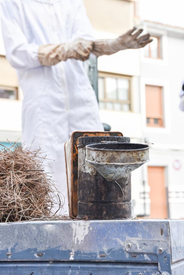 Chiusura di un fumatore di api sopra un alveare e in background gli apicoltori che si preparano. fotografia stock libera da diritti