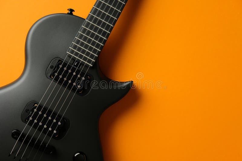 Chiusura di una elegante chitarra elettrica nera con picchetti e corde contro un vibrante dorso arancione fotografie stock libere da diritti