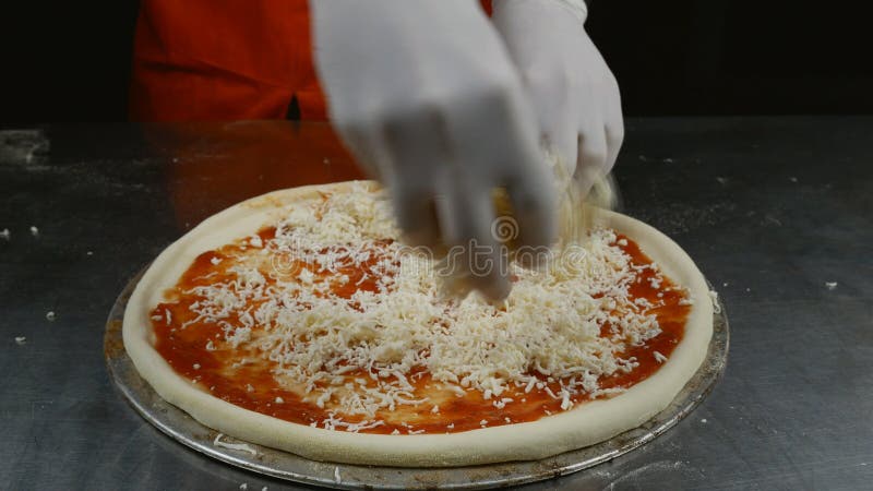 Chiusura di uno chef che spruzza formaggio su pasta per pizza in una pizzeria tradizionale italiana. pizza da cucina.