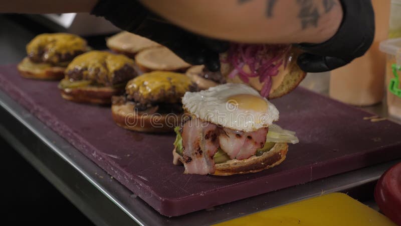 Chiusura di uno chef in guanti che mette panini con salsa su hamburger con uova fritte video d archivio