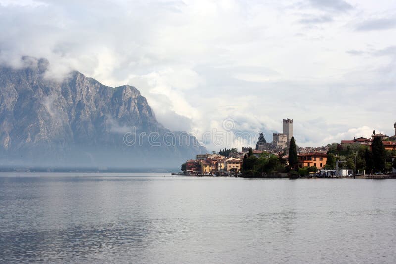 Morning italian resort Malcesine in clouds with mountains as a background. Morning italian resort Malcesine in clouds with mountains as a background