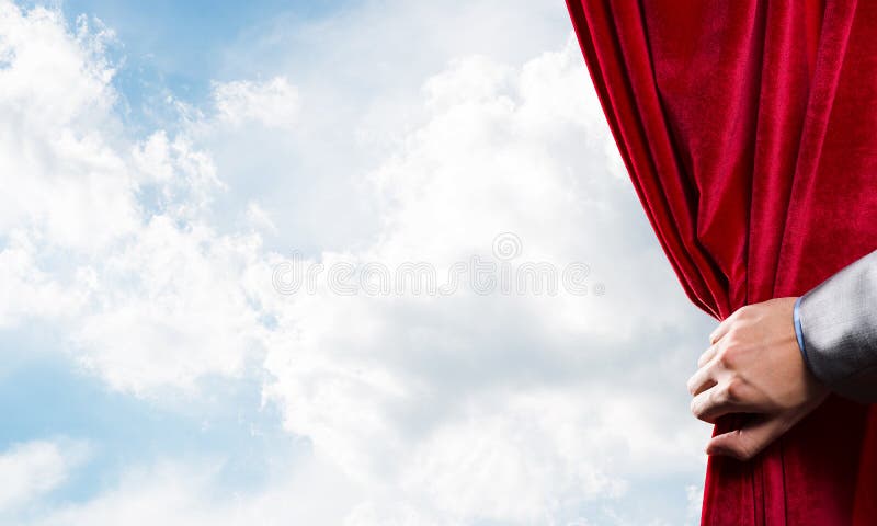 Cloudy landscape behind red curtain and hand holding it. Human hand opens red velvet curtain on blue sky background