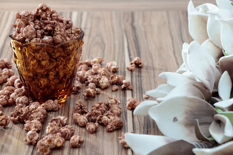 Chocolate aroma popcorn in the yellow glass and on the brown wood table with white flower background