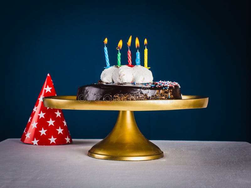 Chocolate cake with five candles and red colored cone cap with s