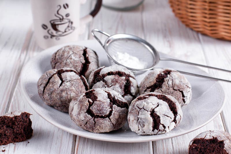 Chocolate crinkle cookies with powdered sugar icing. Cracked chocolate biscuits on white wooden background