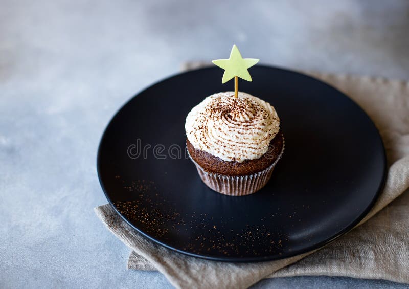 Chocolate cupcake decorated with cream on a light gray background.