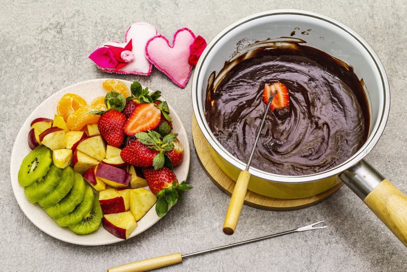 Chocolate fondue. Assorted fresh fruits, two types of chocolate, felt hearts. Ingredients for cooking a sweet romantic dessert.