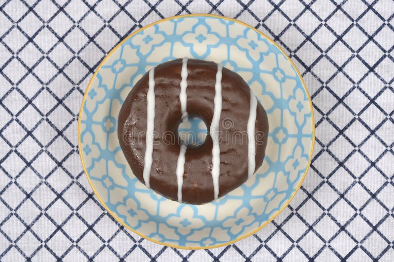 Chocolate glazed donut with white stripes a top down view of icing on blue patterned plate over checkered tablecloth royalty-vrije stock afbeelding