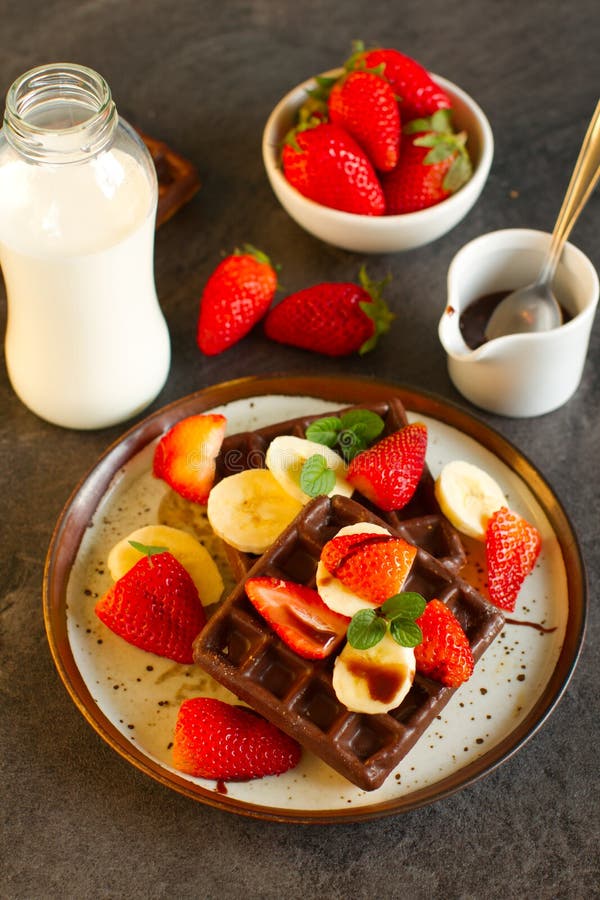Chocolate waffles with fruits on dark background. Chocolate waffles with milk, banans and berries for breakfast royalty free stock image Chocolate waffles with fruits on dark background. Chocolate waffles with milk, banans and berries for breakfast royalty free stock image