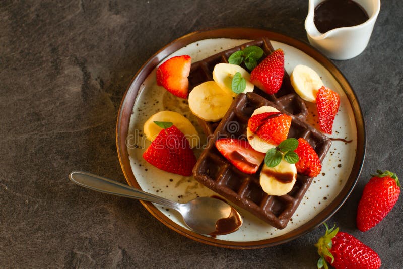 Chocolate waffles with fruit on dark background. Chocolate waffles with milk, banans and berries for breakfast stock image Chocolate waffles with fruit on dark background. Chocolate waffles with milk, banans and berries for breakfast stock image