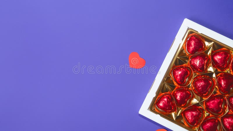 Chocolates en una caja con corazón de amor rojo en forma de chocolate con fondo violeta. color de moda del año 2022 muy peri.