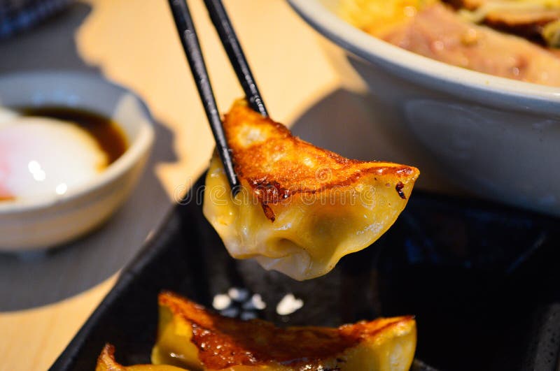 Chopsticks Pick Japanese Style Fried Gyoza Dumplings from a Black Plate