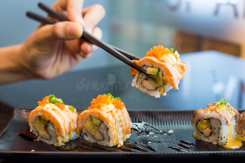 Chopsticks που παίρνουν ένα τμήμα των ρόλων σουσιών, εύγευστα σούσια στο α στοκ φωτογραφίες Chopsticks που παίρνουν ένα τμήμα των ρόλων σουσιών, εύγευστα σούσια στο α στοκ φωτογραφίες