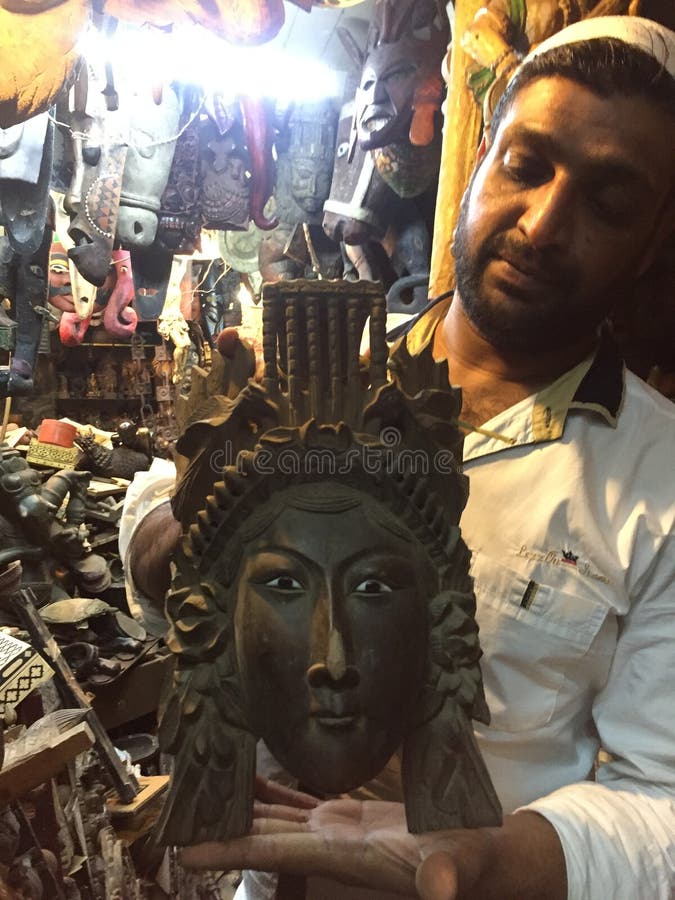 A flea market shop owner hold up an antique wooden mask for sale at Chor Bazaar - Mumbai`s Flea Market. A flea market shop owner hold up an antique wooden mask for sale at Chor Bazaar - Mumbai`s Flea Market.