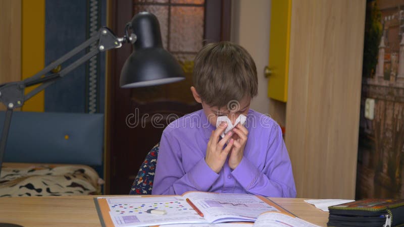 Chora chłopiec dmucha jego w pieluchę nos podczas gdy siedzący przy stołem w domu