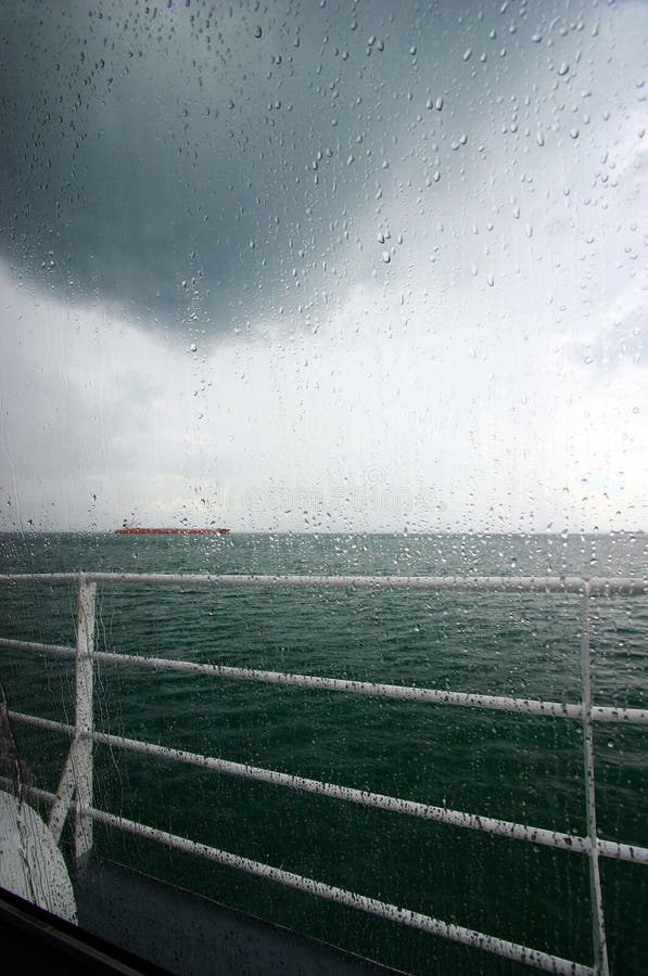 A rainy sea view taken on board a ferry boat, with droplets of rain on the window. View of dark green sea with storm clouds hanging overhead, and a red ship on the far horizon. Cool refreshing feeling and nice mood. Composed with copy space for text, words, letterings etc. Photograph of landscape or seascape. Bad or unexpected weather during travels. A rainy sea view taken on board a ferry boat, with droplets of rain on the window. View of dark green sea with storm clouds hanging overhead, and a red ship on the far horizon. Cool refreshing feeling and nice mood. Composed with copy space for text, words, letterings etc. Photograph of landscape or seascape. Bad or unexpected weather during travels.