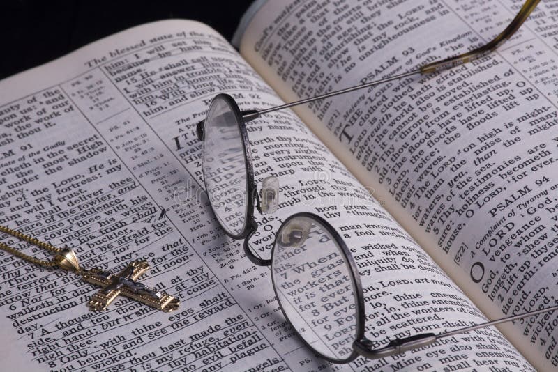 Glasses laying across a Bible turned to psalms with a gold crucifix laying on the page. Passages are underlined from years of study. Glasses laying across a Bible turned to psalms with a gold crucifix laying on the page. Passages are underlined from years of study.