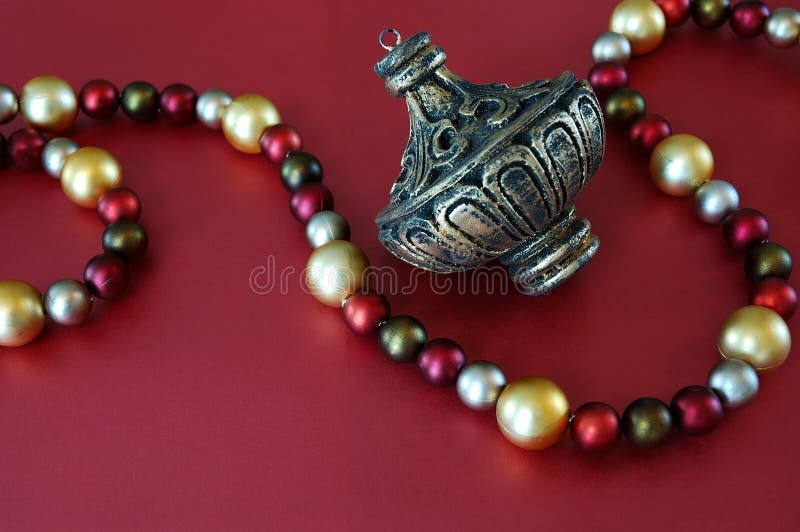 Vintage Christmas ornament and holiday bead garland in shades of red, green and gold over red paper background.