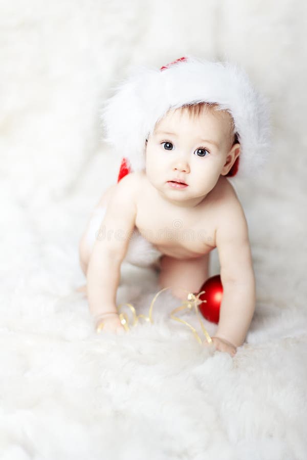 Christmas baby in red Santa Claus hat over white fur go on hands and knees. Christmas baby in red Santa Claus hat over white fur go on hands and knees