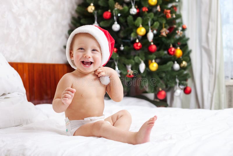 Christmas baby in santa hat sitting on bed