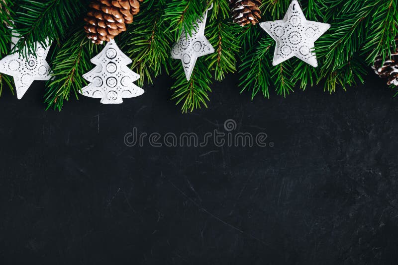 Christmas background with fir branches and cones white festive stars on a dark concrete background. Top view, copy space