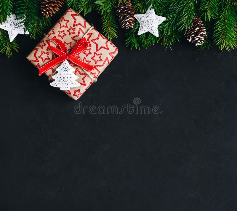 Christmas background with fir branches and a gift box with a red bow on a dark concrete background. Top view, copy space