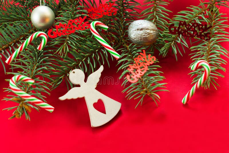 Christmas background on a red background with a Christmas tree branch decorated with a figure of a white angel, sweets and shiny C