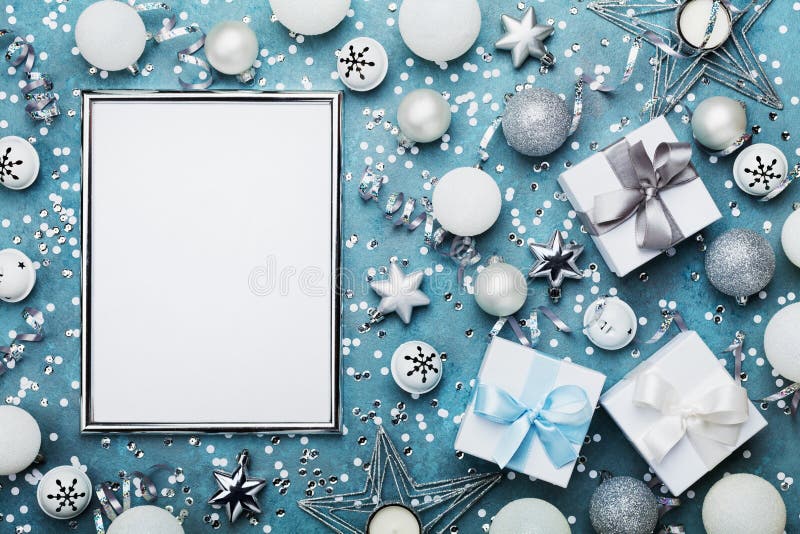 Christmas background. Silver frame with xmas decoration, gift box, confetti and sequins on vintage blue table top view. Flat lay.