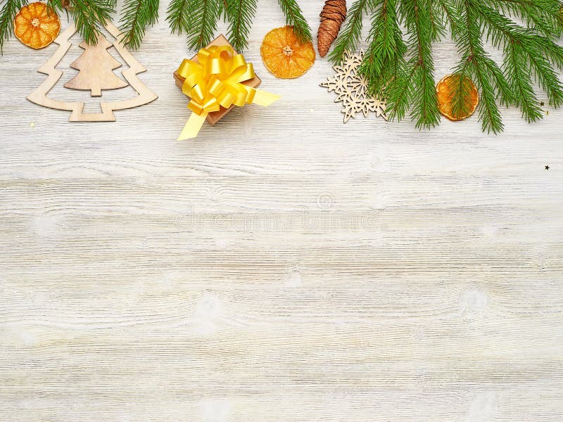 Christmas background. Small Kraft box gift with yellow bow. Fir-tree branches, wooden toys, pinecone, orange slices on a white