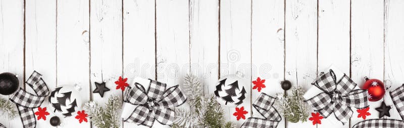 Christmas banner of black and white checked buffalo plaid ribbon, gifts and ornaments, above view bottom border on a white wood ba
