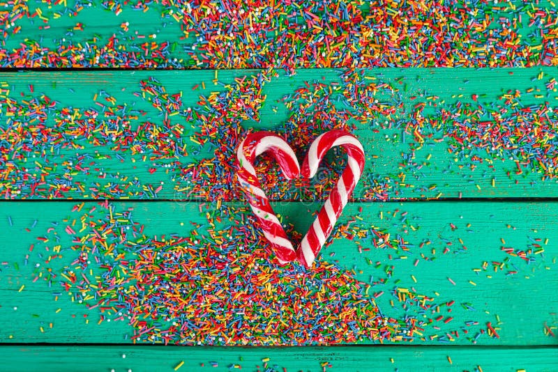 Christmas cane in a heart shape and color sprinkling on turquoise wooden background