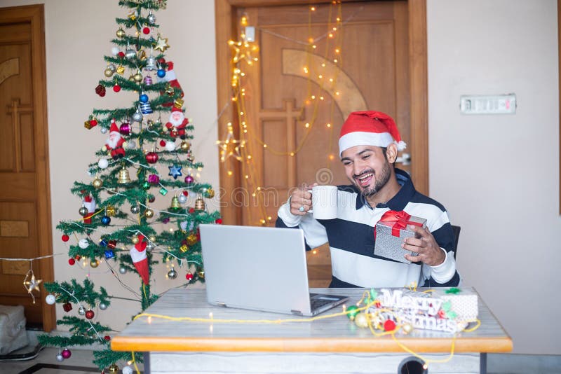 Christmas celebration 2020, Young cheerful indian man congratulating virtually online on laptop computer showing gift present,. Pandemic, new year, holiday stock photos